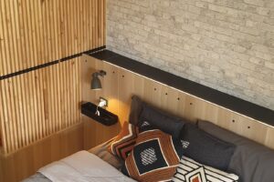 Letto con testiera personalizzata e rivestimento in legno verticale – progetto per camera bohemienne con carta da parati effetto mattone