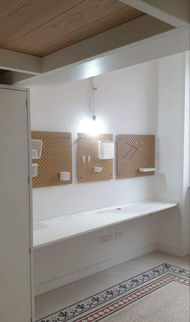 Postazione studio con pannelli accessori IKEA montati a parete, scrivania sospesa e pavimento con cementine decorative.